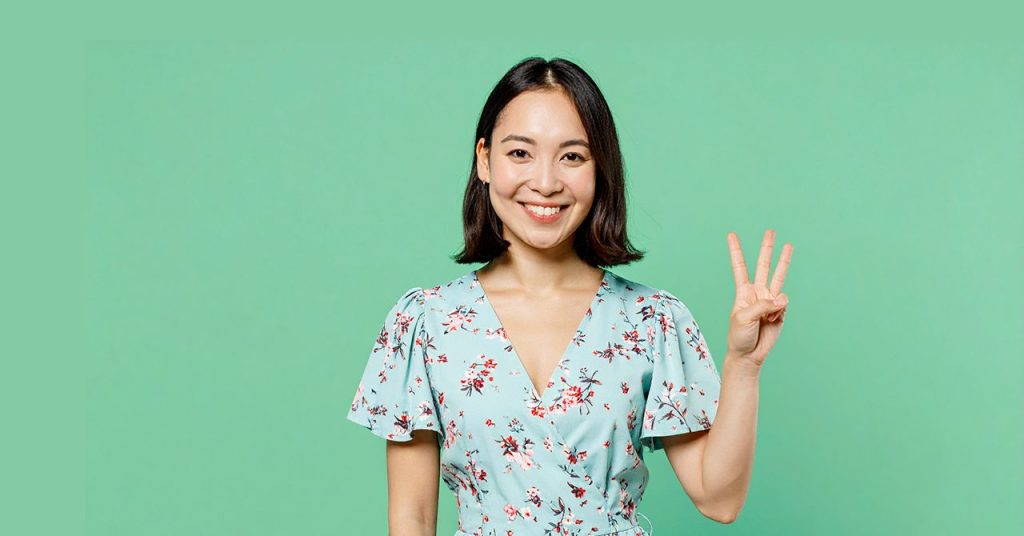 笑顔で3本の指を立てる若い女性。グリーンの背景に、花柄のワンピース姿で『3つのポイント』を伝えるイメージ。