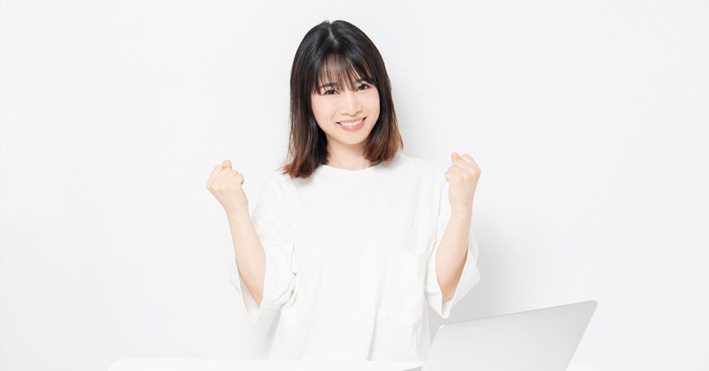 ガッツポーズをしながら笑顔を見せる若い女性。目標達成や成功の喜びを表現したポジティブな雰囲気。