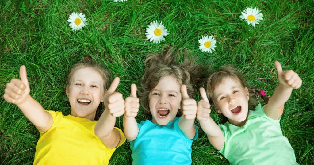 3人の女の子が芝生に寝転んで親指を立てている画像